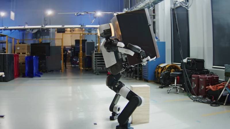 Humanoider Roboter trägt ein Bauteil durch eine Werkshalle (Symbolbild, Quelle: Humanoid Guide)