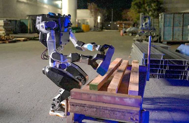 Humanoid von Noble Machines hebt auf einer Baustelle ein Holzbrett an (Quelle: The Robot Report)