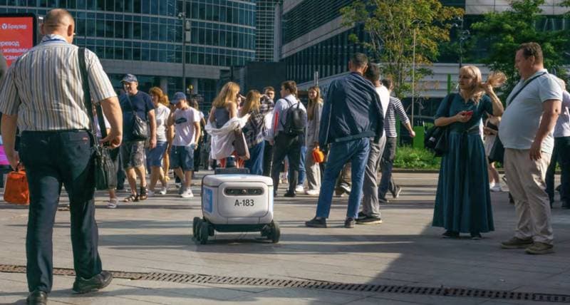 Kleiner Roboter zwischen Fußgängern in einer Innenstadt (Symbolbild)