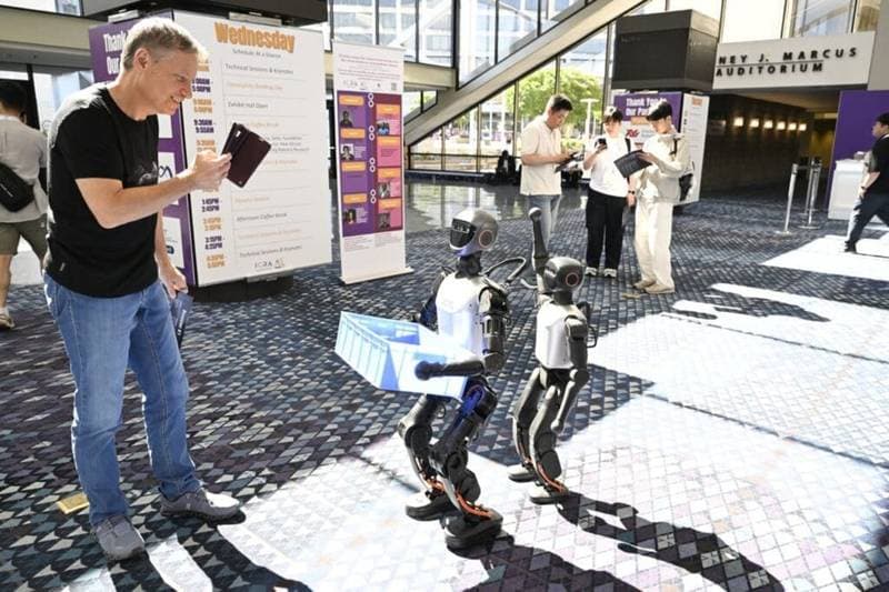Humanoide Roboter tragen eine Kiste in einer Werkshalle (Foto: Humanoid Guide)
