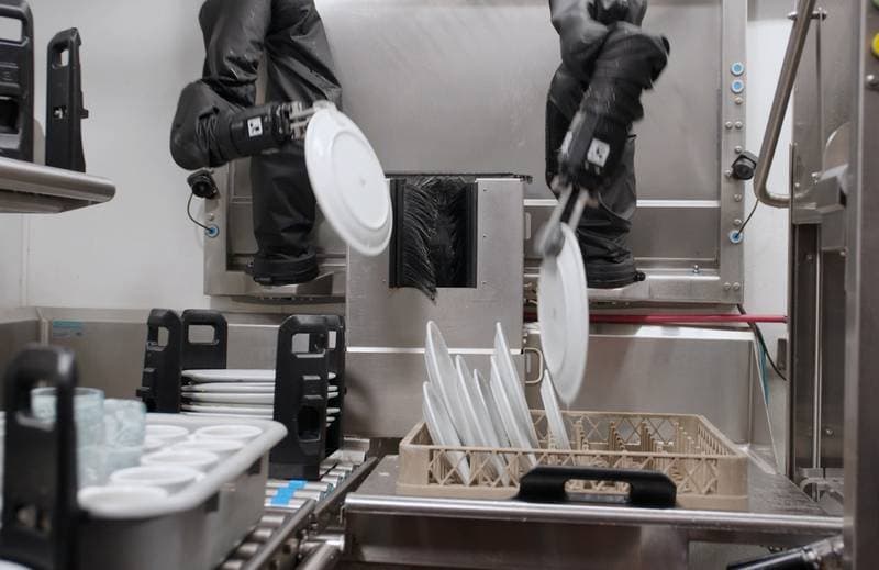 Zwei Roboterarme räumen Teller in einen Geschirrspüler in einer Spülküche