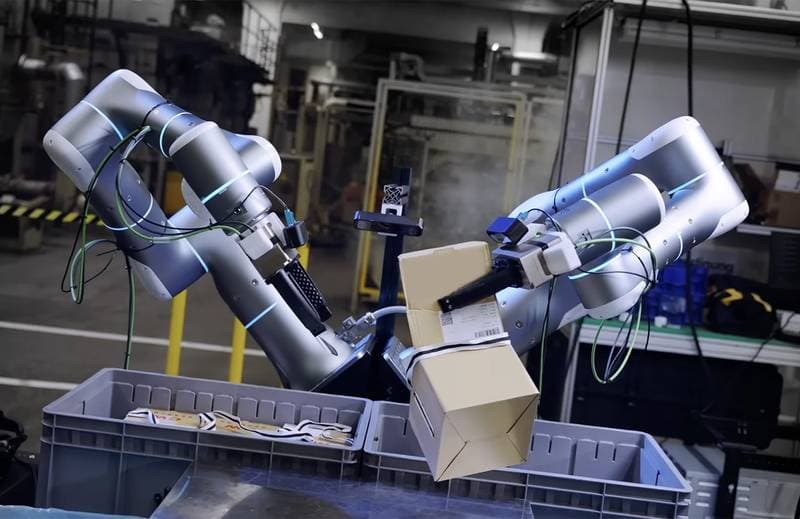 Zwei Roboterarme packen einen Karton