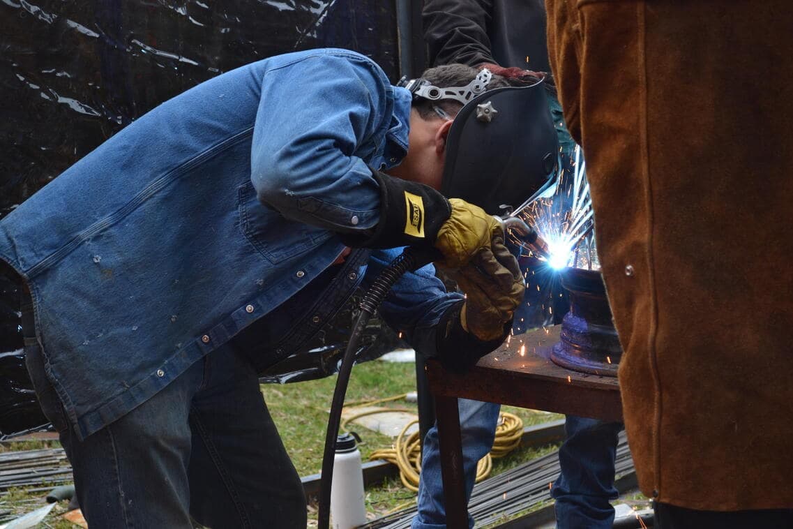 Schweißer mit Helm und ESAB-Handschuhen setzt einen Lichtbogen an ein Metallbauteil (Quelle: ESAB)