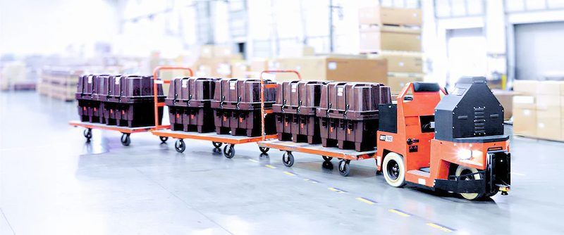 Ein autonomer Transportroboter zieht Wagen mit Kisten durch eine Werkshalle Foto: Cyngn