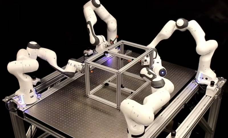 Mehrere Roboterarme bearbeiten eine gemeinsame Aufgabe — Physical AI verteilt Arbeitsaufträge statt fester Programme Que