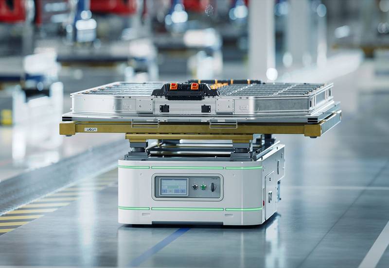 Ein fahrerloses Transportfahrzeug bewegt ein Batteriemodul durch eine Fabrikhalle — solche Spezialisten tragen die erste