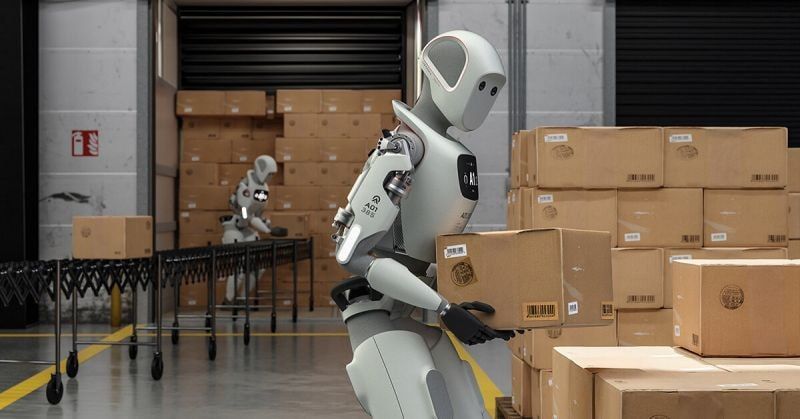 Humanoider Roboter greift einen Karton aus einem Stapel, im Hintergrund ein zweiter am Rollgang Symbolbild